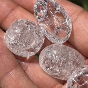 May include: Four clear quartz crystal tumbled stones with a cracked or fractured surface. The stones are smooth and polished.