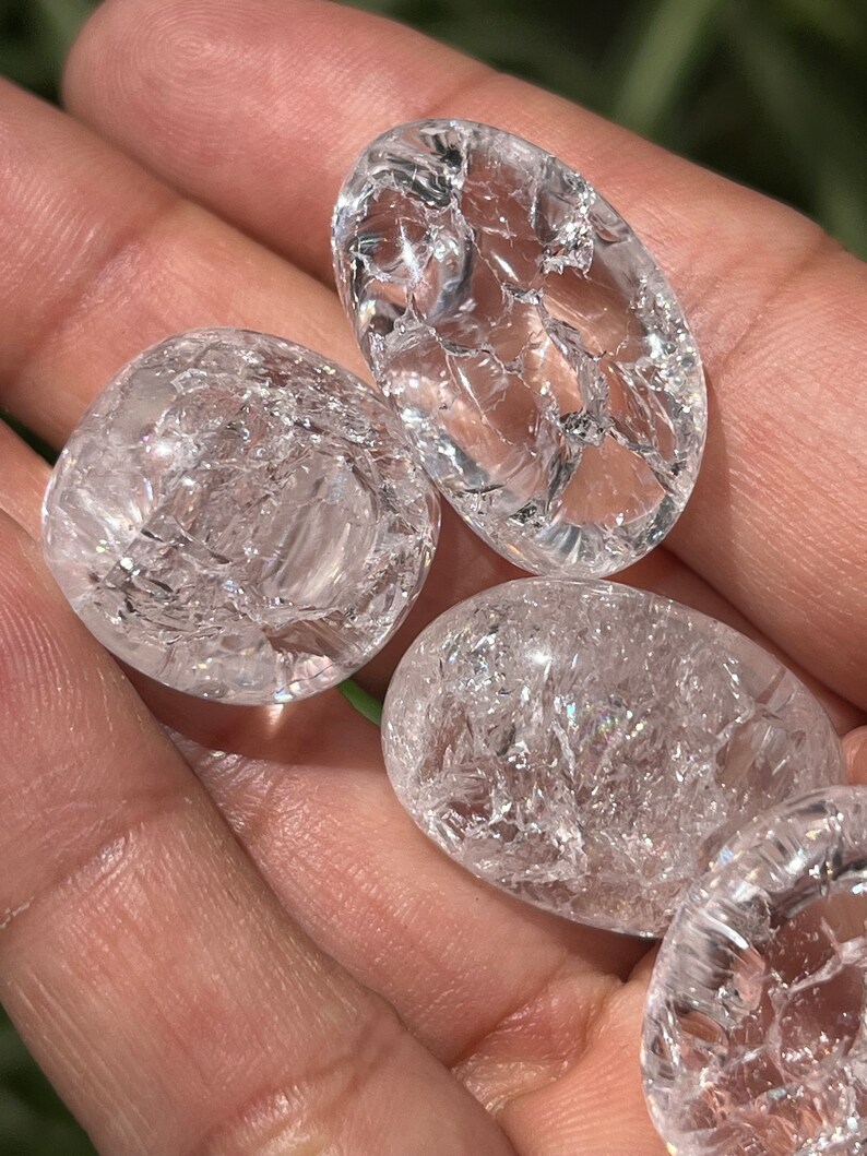 May include: Four clear quartz crystal tumbled stones with a cracked or fractured surface. The stones are smooth and polished.