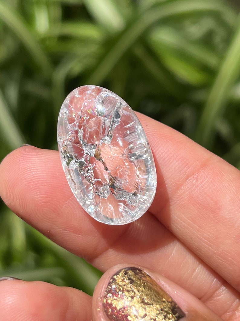 May include: A clear quartz crystal with a unique, cracked texture. The crystal is oval-shaped and has a smooth, polished surface.