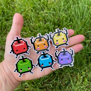 May include: Seven colourful pixelated character stickers with different facial expressions. The characters are red, orange, yellow, green, blue, purple, and white.