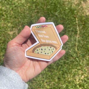 Puede incluir: Una pegatina de una caja de pizza con una rebanada de pizza dentro. La caja es marr&oacute;n con un patr&oacute;n de cuadros rojos y verdes en la parte superior. El texto en la pegatina dice "Aprend&iacute; eso del repartidor de pizza."
