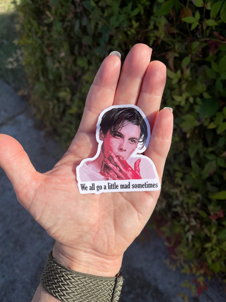 May include: A sticker featuring a portrait of a man with dark hair and a white shirt. His hands are covered in red paint. The sticker has the text "We all go a little mad sometimes" printed below the portrait.