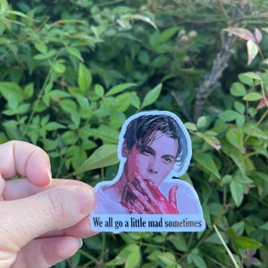 May include: A sticker featuring a man with dark hair and a white shirt. His hands are covered in red paint. The sticker has the text "We all go a little mad sometimes".