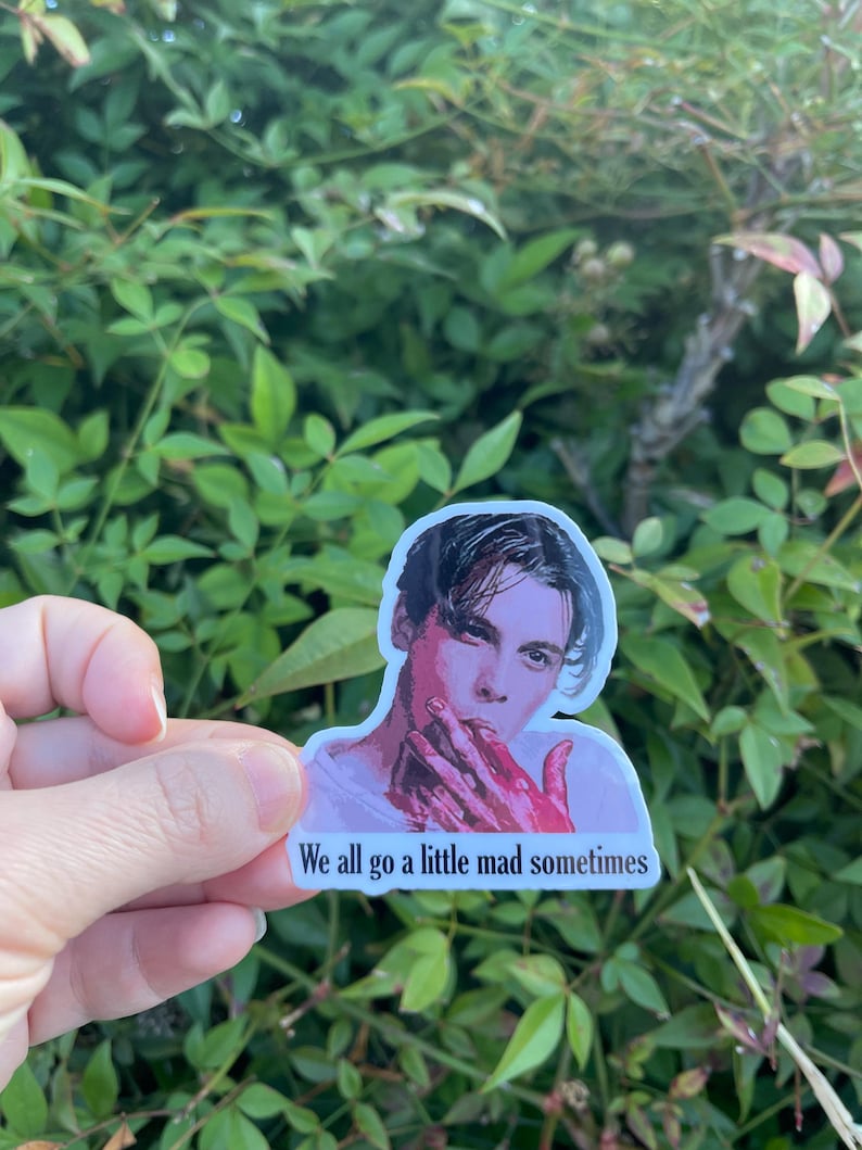 May include: A sticker featuring a man with dark hair and a white shirt. His hands are covered in red paint. The sticker has the text "We all go a little mad sometimes".