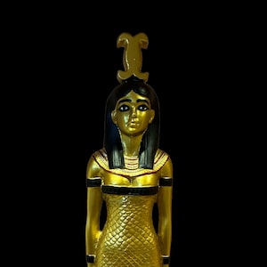 May include: A gold statue of an Egyptian goddess with a snake headdress and a golden dress with a scale pattern.
