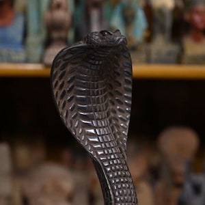 May include: A black wooden cobra statue with a detailed, textured surface. The cobra is in a coiled position with its head raised and hood expanded.