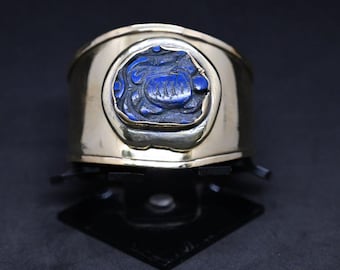 May include: A gold cuff bracelet featuring a blue stone inlay. The stone is carved with a floral design.