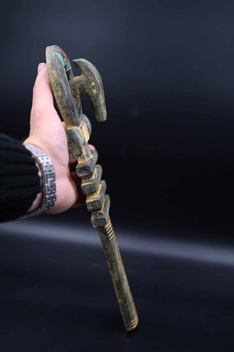 Puede incluir: Un bast&oacute;n de madera con una cabeza de animal tallada en la parte superior. El bast&oacute;n est&aacute; pintado en tonos de marr&oacute;n, negro y verde.