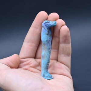 Puede incluir: Una peque&ntilde;a figura azul verdosa de un dios egipcio con cuerpo humano y cabeza de halc&oacute;n.