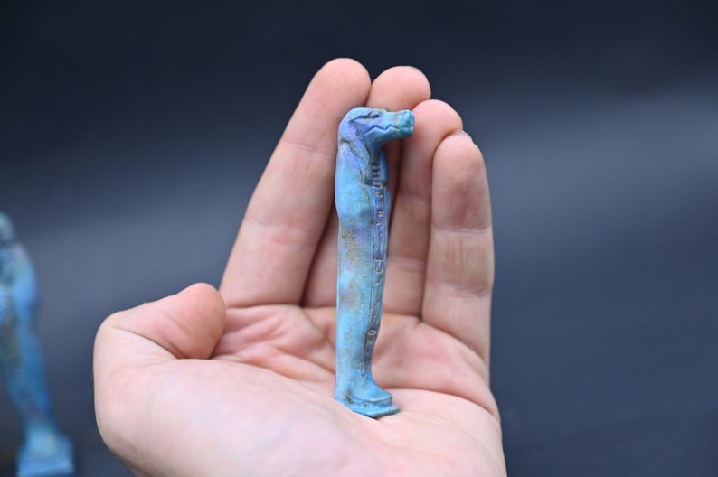 Puede incluir: Una peque&ntilde;a figura azul verdosa de un dios egipcio con cuerpo humano y cabeza de halc&oacute;n.