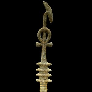 K&ouml;nnte beinhalten: Eine rostige Metallsculptur eines Ankh, ein altes &auml;gyptisches Symbol des Lebens, mit einer gebogenen Spitze und einem mehrschichtigen Sockel.