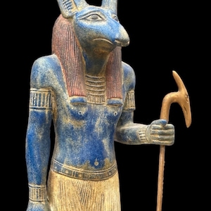 May include: A blue and gold statue of the Egyptian god Anubis, depicted as a jackal-headed human with a staff in his right hand.