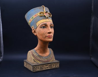 May include: A bust of Queen Nefertiti, an ancient Egyptian queen, with a blue and gold headdress and a detailed necklace. The bust is made of painted resin and is on a square base with hieroglyphics.