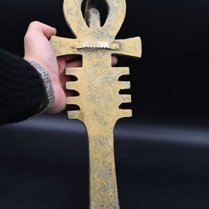 Puede incluir: Una decoraci&oacute;n de pared de Ankh de color dorado con una superficie texturizada. El Ankh es un s&iacute;mbolo de la vida en la cultura egipcia antigua.