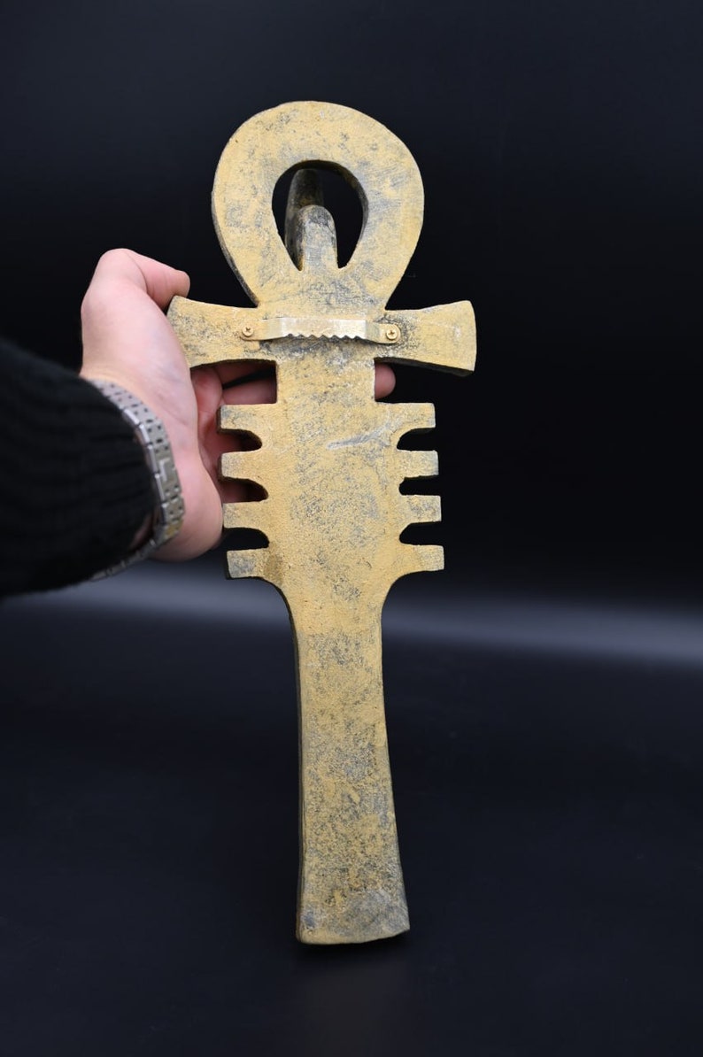 Puede incluir: Una decoraci&oacute;n de pared de Ankh de color dorado con una superficie texturizada. El Ankh es un s&iacute;mbolo de la vida en la cultura egipcia antigua.