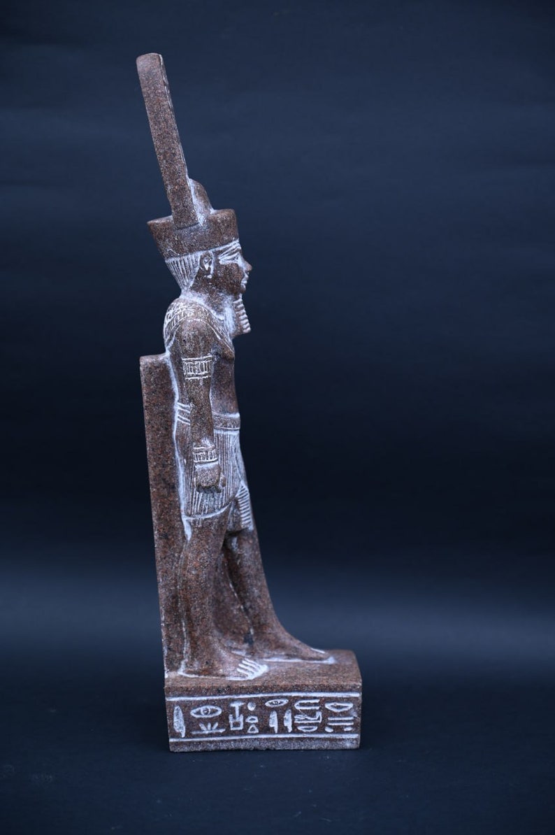 Puede incluir: Una estatua de piedra marr&oacute;n de un fara&oacute;n egipcio de pie sobre una base con jerogl&iacute;ficos. El fara&oacute;n lleva un alto tocado y una falda.