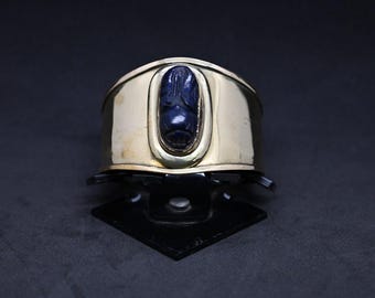 May include: A gold cuff bracelet featuring a blue scarab beetle design.