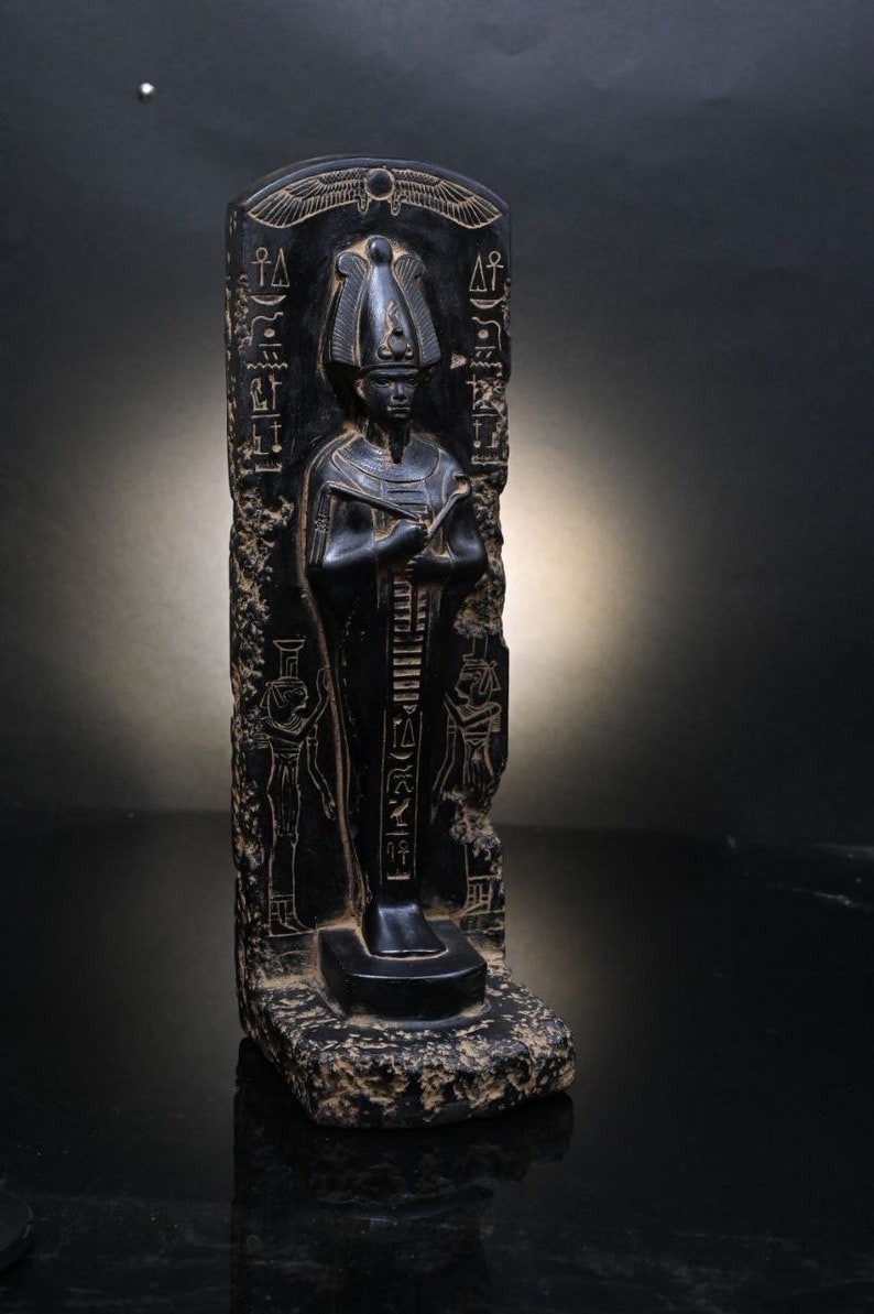 Puede incluir: Estatua de piedra negra de un fara&oacute;n egipcio con jerogl&iacute;ficos tallados en la piedra. El fara&oacute;n lleva una corona alta y sostiene un bast&oacute;n.