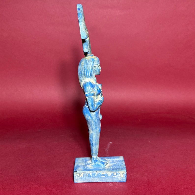 May include: A blue ceramic statue of an Egyptian goddess with a tall headdress. The statue is standing on a rectangular base with hieroglyphs.