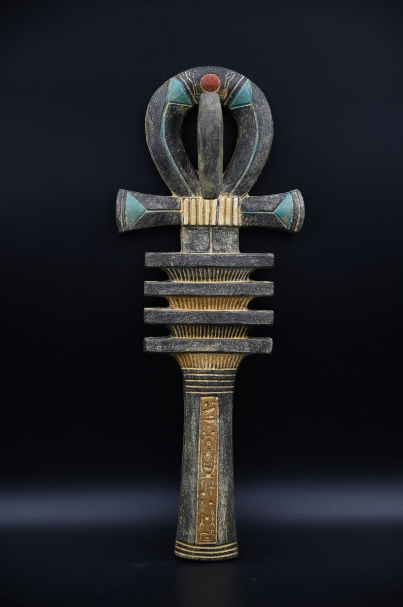 Puede incluir: Un Ankh de madera negro y dorado, un antiguo s&iacute;mbolo egipcio de la vida, con un punto rojo en la parte superior y acentos azules y verdes. El Ankh est&aacute; decorado con jerogl&iacute;ficos.