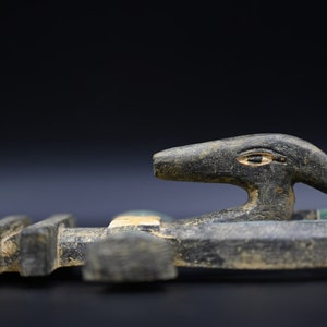 Puede incluir: Una escultura de madera negra de un dios egipcio con cabeza humana y cuerpo de p&aacute;jaro. La escultura est&aacute; decorada con pintura azul y verde.