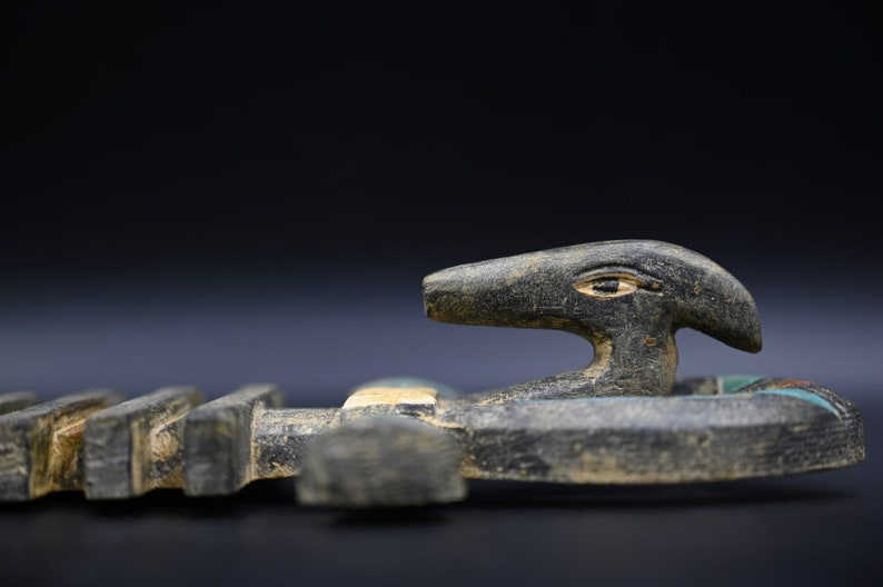 Puede incluir: Una escultura de madera negra de un dios egipcio con cabeza humana y cuerpo de p&aacute;jaro. La escultura est&aacute; decorada con pintura azul y verde.