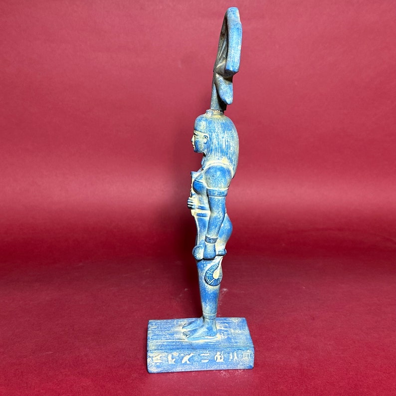 May include: A blue ceramic statue of an Egyptian goddess with a headdress and a cobra on her arm. The statue is standing on a base with hieroglyphics.