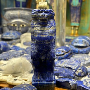 May include: A small blue lapis lazuli statue of a monkey with a crown on its head. The statue is intricately carved and has a detailed face.