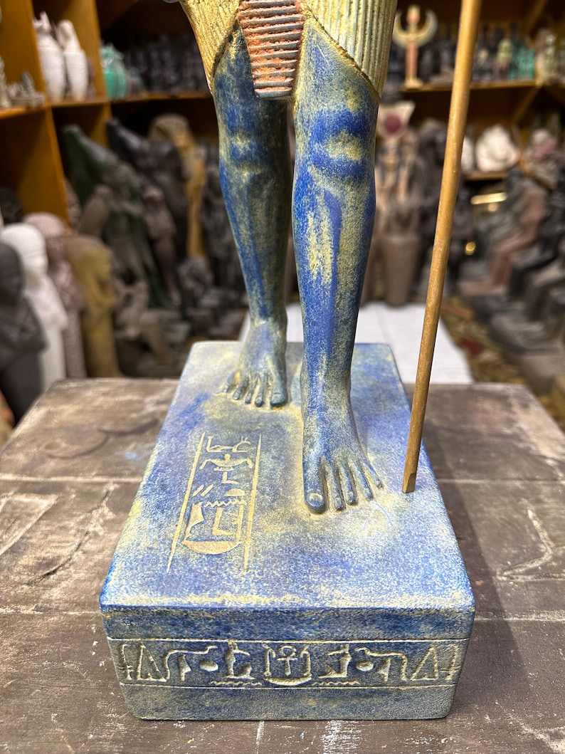May include: A blue and gold Egyptian statue of a standing figure with hieroglyphics on the base. The statue is made of resin and is approximately 12 inches tall.