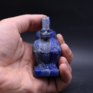 May include: A carved lapis lazuli figurine of a monkey. The monkey is depicted in a seated position with its hands resting on its knees. The figurine is a deep blue color with some lighter veining. The monkey has a detailed face and a tall headdress.