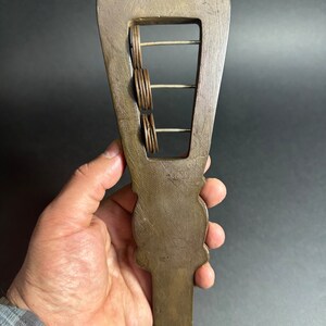 May include: A wooden hand-held musical instrument with a rectangular frame and metal rings that slide up and down the frame. The instrument is brown and has a carved design on the handle.