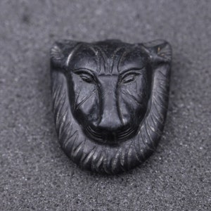 May include: A black carved stone pendant featuring a detailed lion's face with a mane.