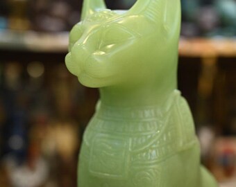 May include: A green jade cat figurine with intricate details and a smooth, polished finish. The cat is sitting upright with its head tilted slightly to the side.
