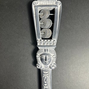 May include: A silver-colored, hand-held musical instrument with a carved female face and a series of metal rings that can be shaken to make a sound. The instrument is decorated with Egyptian-style hieroglyphs.