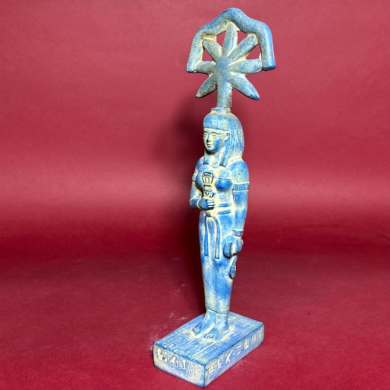 May include: Blue ceramic statue of an Egyptian goddess with a crown and holding a staff. The base of the statue has hieroglyphics.