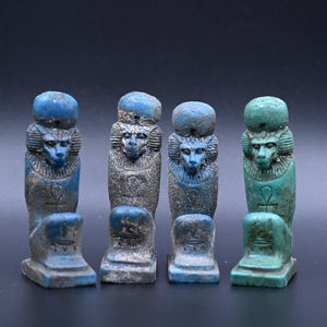 Peut inclure: Quatre petites statues bleues et vertes du dieu égyptien Anubis, chacune avec une tête de chacal et un corps humain. Les statues sont debout sur une surface noire.
