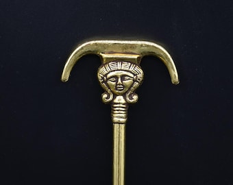 Puede incluir: Un gancho de metal dorado con un diseño de cara decorativo. El gancho tiene una parte superior curva y un tallo largo y delgado.