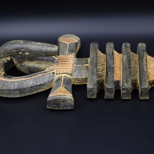 以下が含まれることがあります： 蛇の頭と複雑なディテールが施された、生命の象徴である木製のアンク。アンクは主に濃いグレーで、金と赤のアクセントがあり、長さは約30cmです。