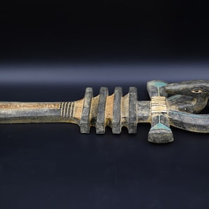 Puede incluir: Un Ankh de madera, un antiguo s&iacute;mbolo egipcio de la vida, con un acabado pintado en negro, marr&oacute;n y dorado. El Ankh es una cruz con un bucle en la parte superior y una cabeza de cobra en la parte inferior.