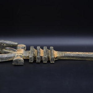 以下が含まれることがあります： ヘビの頭と長方形のハンドルが付いた、彫刻された木製の工芸品。彫刻は主に濃い灰色で、金と赤のアクセントがあります。ヘビの頭は詳細で、ハンドルはテクスチャード加工のデザインになっています。