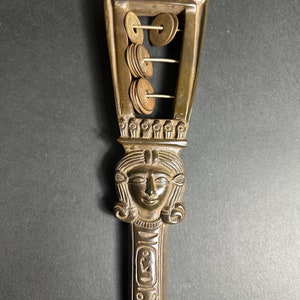 May include: A wooden sistrum with a carved female head and a series of metal discs that rattle when shaken. The sistrum is a musical instrument used in ancient Egypt.