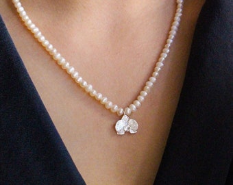 May include: A delicate pearl necklace with a small silver flower pendant. The necklace is made of white pearls and the pendant is a cluster of three silver flowers.