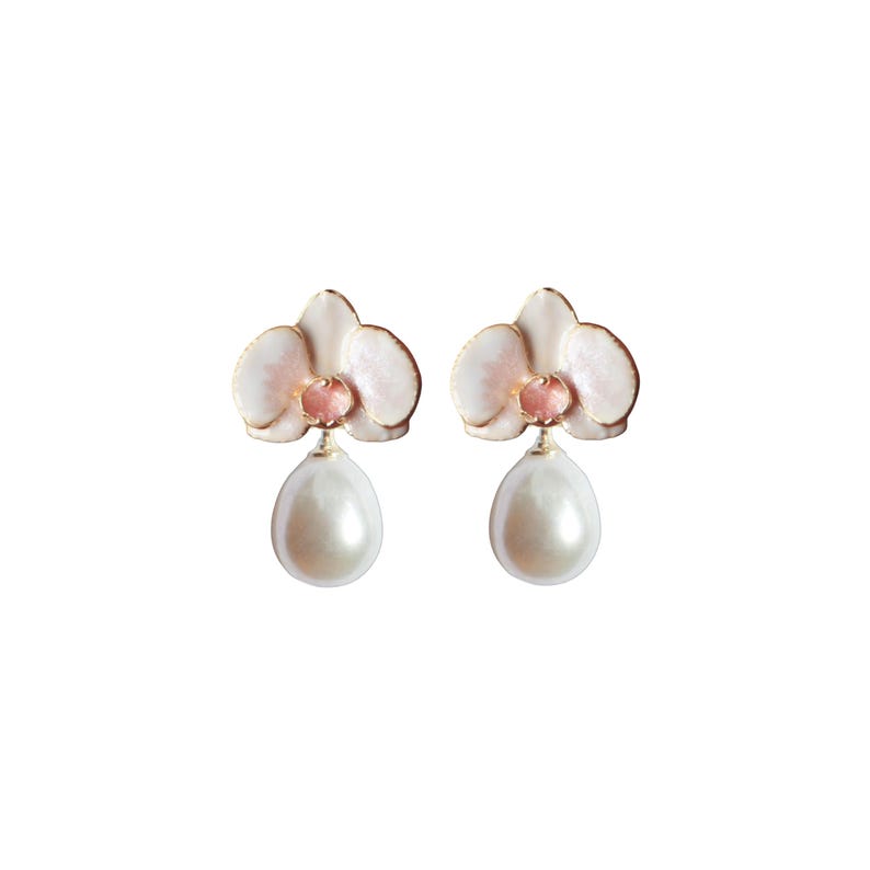 May include: A pair of orchid-shaped earrings. The earrings feature a white and pink floral design with gold-colored trim and a pear-shaped pearl drop. The earrings are set against a white background.