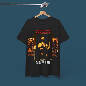 Puede incluir: Camiseta negra con un gráfico de una banda llamada "Front Line Assembly" y el texto "Caustic Grip".