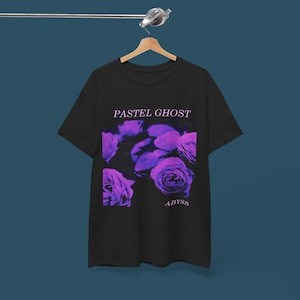 May include: Black t-shirt with a floral design in shades of purple and pink. The text "PASTEL GHOST" is above the floral design, and the word "ABYSS" is below it. The shirt is hanging on a wooden hanger.