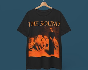 May include: Black t-shirt with an orange graphic of a person standing in front of a group of lions. The text "THE SOUND" is printed in orange above the graphic.