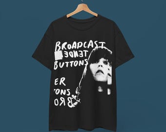 Puede incluir: Camiseta negra con un estampado gráfico blanco de la cara de una mujer y el texto "BROADCAST BUTTONS" en estilo manuscrito.