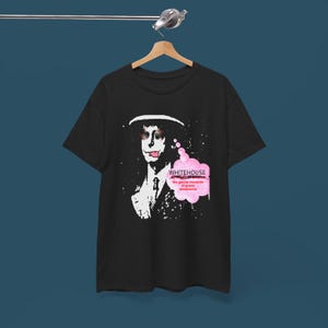 May include: Black t-shirt with a graphic of a person with dog-like features wearing a hat and suit. A pink speech bubble contains the text "WHITEHOUSE the genius invention of power electronics."