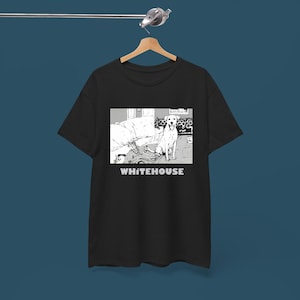 May include: Black t-shirt with a black and white graphic of a dog and the word "WHITEHOUSE" in white. The graphic shows a dog in a room with furniture. The t-shirt is hanging on a wooden hanger.