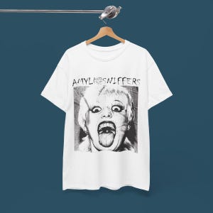 May include: White t-shirt with a black and white image of a woman with her tongue sticking out. The text "Amyl and the Sniffers" is printed above the image.